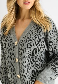Grau gestrickte Strickjacke mit schwarzem Leopardenmuster, ausgestattet mit einem tiefen V-Ausschnitt, goldenen Knöpfen, gerippten Bündchen und lässiger Passform. Strukturierter Stoff.