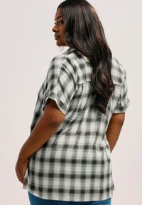 Camicia a quadri grigia e nera, maniche corte, vestibilità ampia, tessuto leggero, con dettaglio della tasca anteriore e orlo curvo.