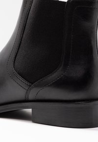 Czarny skórzany botek za kostkę z elastycznymi panelami bocznymi, gładką fakturą, niskim, warstwowym obcasem oraz subtelnymi detalami przeszyć.