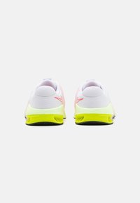 Un paio di scarpe da atletica bianche e giallo neon viste dal tallone con il logo Nike rosso e suole nere etichettate "Hyperlift".