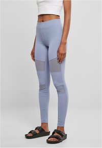 Lyseblå tights med grå mesh-paneler, glatt tekstur, høy midje, tettsittende design, og parret med svarte sandalstraps.