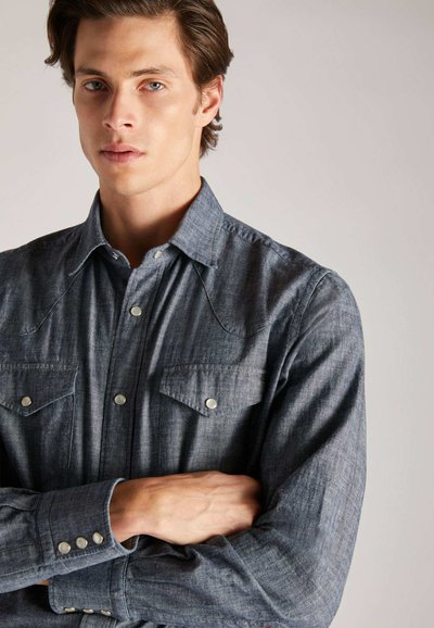 Donkerdenim shirt met een puntige schouderpas, twee borstzakken en drukknoopsluitingen. Bevat een gestructureerde kraag en lange mouwen.