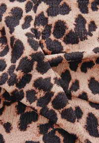 Tkanina s uzorkom leopardove kože ima teksturiranu površinu s bež pozadinom i crnim obrubljenim mrljama, stvarajući jaki kontrast i vizualni interes.