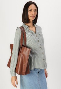 Camicia a righe con maniche lunghe, borsa a spalla in pelle marrone e gonna in denim, con due tasche sul petto e una silhouette rilassata.