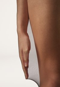 Pantys de red ligeramente transparentes en color bronce, drapeados sobre una mano con una textura suave y ligera. Presentan un acabado liso y uniforme, así como una apariencia translúcida.