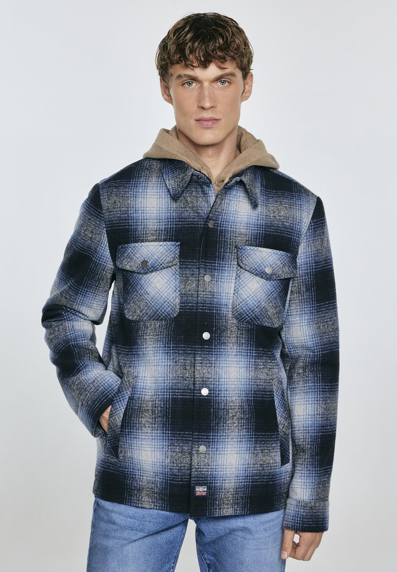 Giacca camicia a scacchi blu e nera con cappuccio tan, due tasche frontali, bottoni a scatto e una texture morbida.