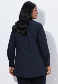 Navy long-sleeve shirt with a collared design, side slits, and buttoned cuffs. Smooth fabric with a fitted shape and slight sheen.