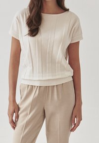 Top di colore crema con texture a coste, maniche corte e vita aderente, abbinato a pantaloni leggeri beige.