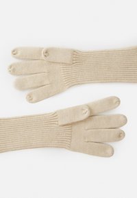 Gants en tricot beige avec compartiments pour chaque doigt, dotés de poignets côtelés et d'une texture douce pour la chaleur et le confort.