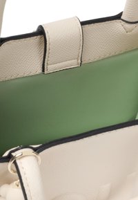 Biały torebka skórzana o fakturze z zielonym wnętrzem i czarnymi akcentami. Posiada zapięcie na klapkę oraz okrągłe elementy metalowe.