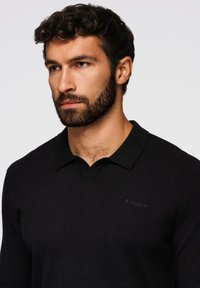 Polo shirt nero a maglia con scollatura a V, dotato di un logo ricamato discreto sul lato sinistro del petto. Texture morbida e vestibilità sartoriale.
