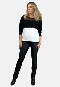 Czarny i biały top z siateczkowym wierzchem, dopasowane do ciała z ćwiekowanym akcentem wzdłuż szwu, w połączeniu ze sleek czarnymi spodniami i botkami.