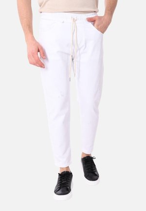 Pantaloni casual bianchi con vita elasticizzata e cordino, dotati di tasche e leggeri strappi. Indossati con sneakers nere.