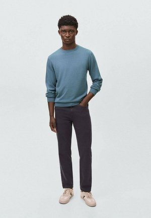 Maglione azzurro, pantaloni scuri e sneakers beige. Il maglione ha un collo rotondo e maniche lunghe; i pantaloni sono slim-fit con una texture liscia.