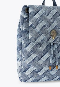 Zaino in denim intrecciato nelle tonalità di blu con chiusura a patta, caratterizzato da un accento decorativo a forma di uccello in metallo e spallacci regolabili a cordoncino.