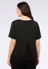 Maglietta nera a maniche corte con scollatura rotonda e spacco dietro. L'orlo inferiore presenta un'accento in pizzo. Tessuto morbido e liscio.