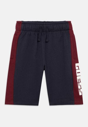 Navy shorts with red side panels, elastic waistband, adjustable drawstring, and white "GUESS" logo on the left leg. Smooth cotton blend fabric.