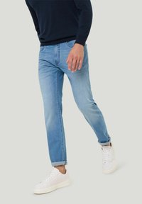 Lichtblauwe denim jeans met een rechte pasvorm, vervaagd uiterlijk, opgerolde mouwen en een subtiel zakontwerp, gecombineerd met witte sneakers.