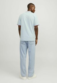 Polo shirt azzurro chiaro con dettagli rossi a contrasto sul colletto e sulle maniche, abbinato a jeans in denim chiaro e sneakers bianche.