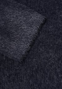 Tissu doux et duveteux gris foncé avec un bord plié montrant la texture et les fibres en gros plan.