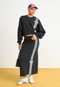 Melna kropta sporta krekls ar baltām Adidas svītrām un logo, kombinēts ar garu melnu svārku ar atbilstošām svītrām un logo. Baltas čības.