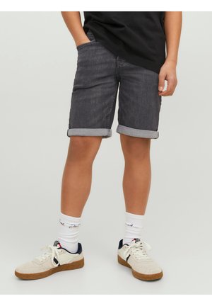 Szare dżinsowe szorty z podwiniętymi nogawkami, w połączeniu z białymi sneakersami z granatowymi akcentami i wzorzystymi skarpetkami, noszone z czarną koszulką.