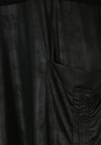 Schwarzes Lederkleidungsstück mit strukturierter Oberfläche, einer seitlichen Tasche mit Raffung und einer glatten Oberfläche.