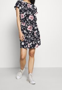 Robe navy à motif floral avec des manches courtes, taille à cordon et tissu léger, assortie à des sneakers hautes blanches.