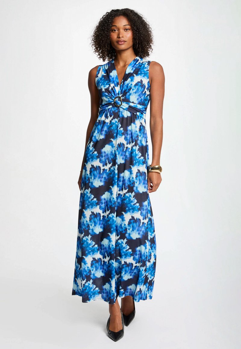 Robe maxi en motif floral bleu et blanc, sans manches avec un corsage plissé. Présente un accent circulaire à la taille.