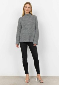 Grå stickad polotröja med lös passform och ribbad textur, kombinerad med smala svarta jeans och sandaler med silverklack.