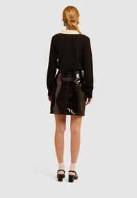 Maglione nero in maglia con un colletto crema, abbinato a una mini gonna nera in pelle lucida. Il modello indossa calze leggere e scarpe con tacco spesso.