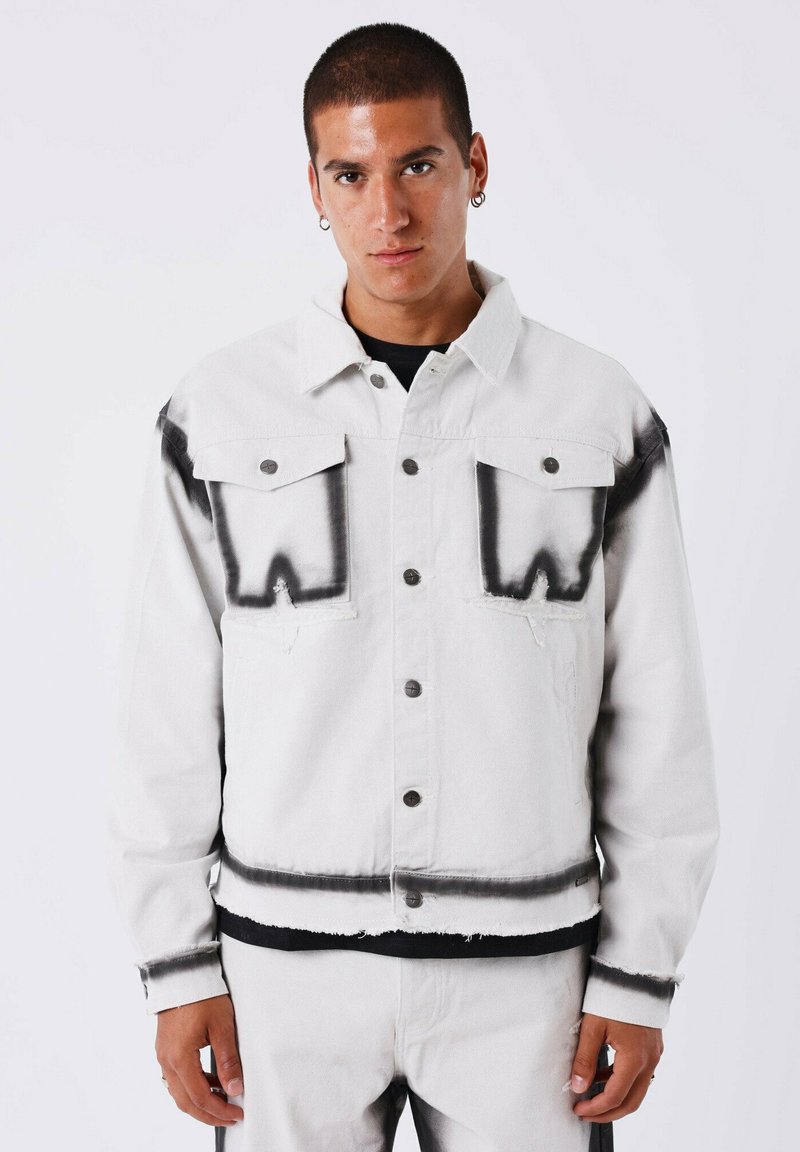 Witte denim jacket met zwarte spuitverf-achtige accenten, voorzien van knoopsluitingen en twee borstzakken. Versleten zoom en manchetten.