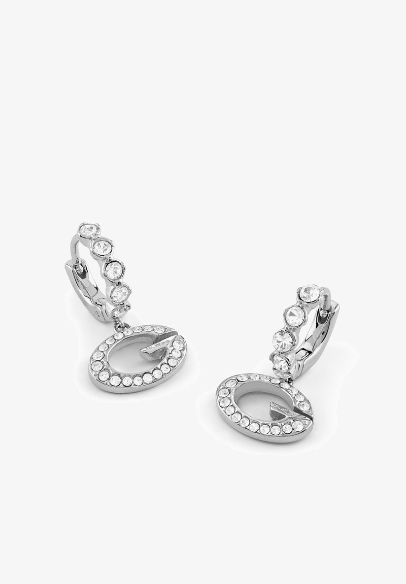 Boucles d'oreilles créoles en argent avec des pierres précieuses transparentes et des pendentifs ovales suspendus incrustés de petites pierres transparentes sur fond blanc.