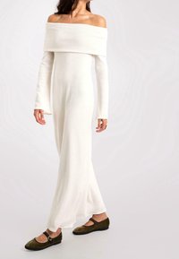 Robe blanche longue décolletée avec des manches longues, en tissu doux. Associée à des ballerines en daim vert olive avec une sangle sur le pied.