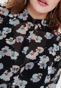 Czarna, przezroczysta bluzka z kwiatowym wzorem w pastelowych kolorach. Posiada kołnierzyk, zapięcie na guziki z przodu oraz czarne guziki. Teksturowany materiał i krótkie rękawy.
