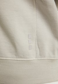 Sudadera de color gris claro con un tejido texturizado, dobladillo acanalado y tres pequeños acentos rectangulares en el lateral. Diseño simple y funcional.