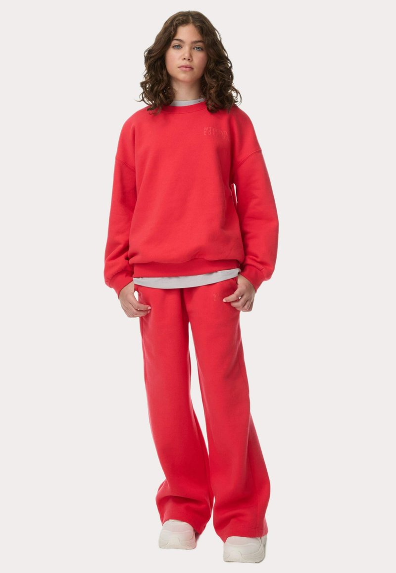Rød sweatshirt og matchende bukser lavet af blødt stof. Sweatshirten har rund hals og løstsiddende pasform. Bukserne har en afslappet silhuet og høj talje.