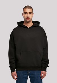 Black oversized hoodie with a front pocket, drawstring hood, and ribbed cuffs, paired with blue denim jeans. Smooth texture, casual design.