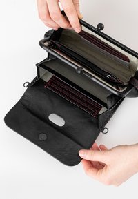 Schwarzes Lederportemonnaie mit Reißverschluss, roten Akzenten und einem gestreiften Innenraum. Es verfügt über mehrere Fächer und einen Druckknopfverschluss.