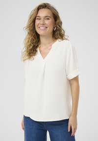 Blusa blanca de manga corta con escote en V, con un frente plisado y mangas enrolladas. Tejido texturizado con un diseño fluido.