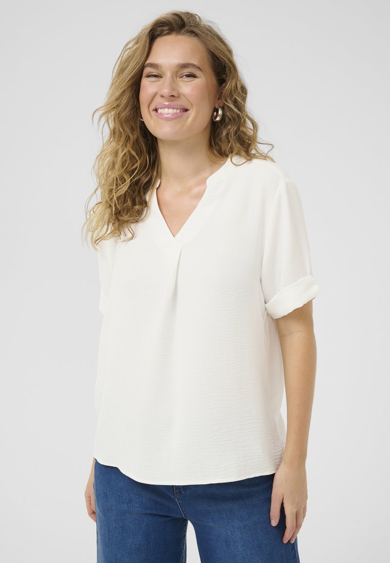 Blusa blanca de manga corta con escote en V, con un frente plisado y mangas enrolladas. Tejido texturizado con un diseño fluido.
