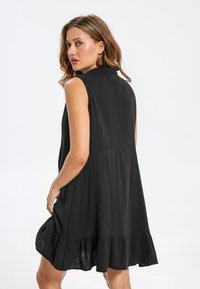 Robe sans manches noire en tissu léger, avec une surface texturée, un ourlet évasé et deux poches latérales.