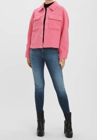 Lyserød fleecejakke med krave, to frontlommer og knaplukning, parret med blå skinny jeans og sorte platform støvler.