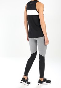 Top deportivo negro sin mangas con franjas blancas; mallas grises con secciones texturizadas en negro y diseño ajustado; zapatillas deportivas negras.