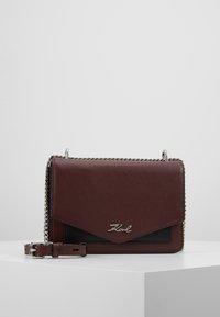 Bordeaux læder crossbody taske med kædestrop i sølvfarve og logo-detalje. Har en kuvertflap og tekstureret overflade. Kompakt design.