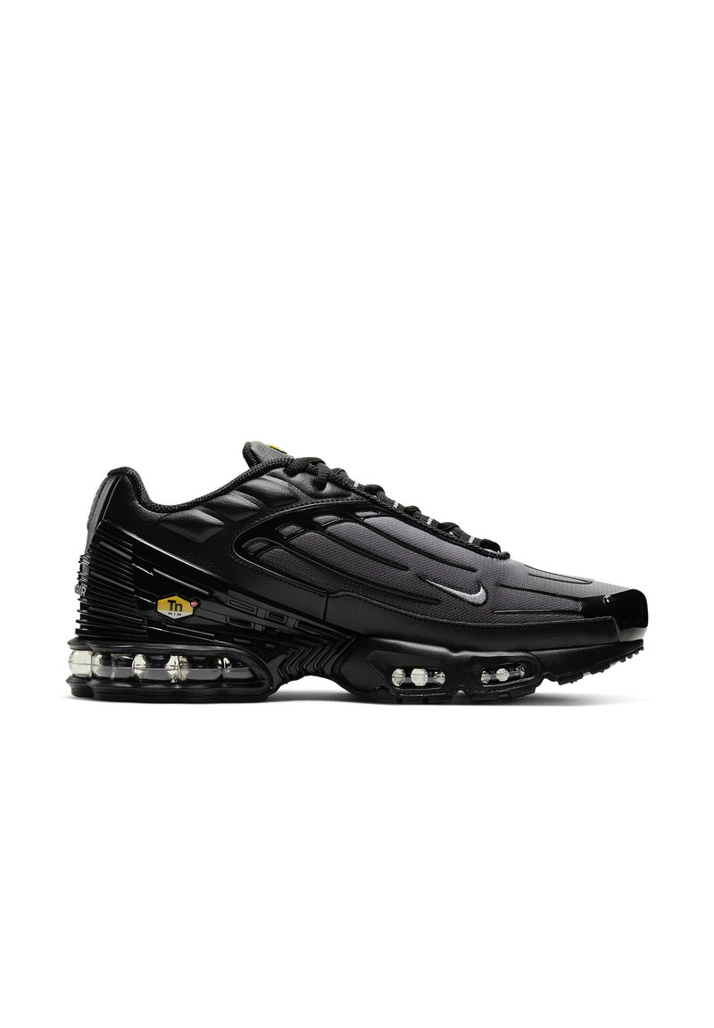 Zapatillas deportivas negras con un upper texturizado, forma curvada y amortiguación de aire visible en la suela. Presenta un logo de acento amarillo.