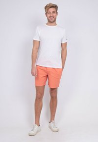 T-shirt en coton blanc associé à un short pêche et des baskets blanches. Le short présente un design à l'avant plat, et le T-shirt a des manches courtes.