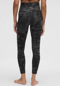 Černé legíny s vysokým pasem, zdobené složitým tmavým květinovým vzorem, vyrobené z měkkého materiálu, s těsným střihem a délku ke kotníkům.