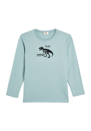 Valkoinen pitkähihainen t-paita pehmeästä kankaasta, jossa on musta dinosauruksen grafiikka ja teksti "WILD ZONE TYRANNOSAURUS VAALEA JA VOIMAKAS."