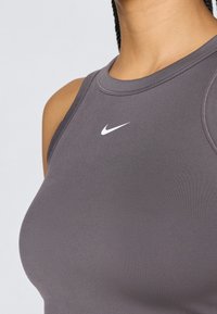 Haut sans manches gris Nike avec un logo blanc, texture lisse, design racerback et silhouette ajustée avec coutures plates.